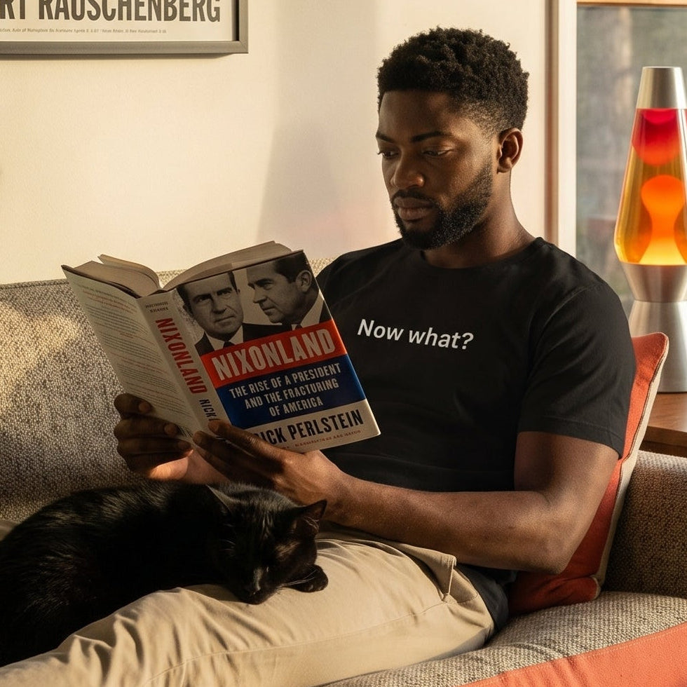 Now What? retro-inspired graphic tee worn by man on mid-century modern sofa reading Nixonland with black cat — Galactic Ink Club