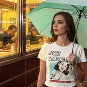 Resist Complacency retro-inspired graphic tee worn by woman outside diner in rain with teal umbrella — Galactic Ink Club