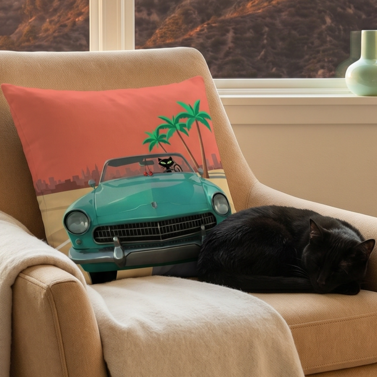 A beige armchair in a real interior setting with a window and outdoor hillside view, featuring a printed throw pillow with a turquoise convertible car and palm trees. A black cat is sleeping on the chair.
